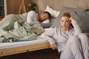 Frau wirkt nachdenklich am Bettrand, Symbolbild für sexuelle Angststörungen in der Partnerschaft.