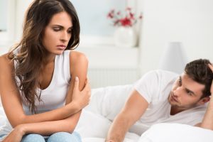 Traurige Frau und besorgter Mann auf dem Bett – Beziehungskonflikt oder Paarprobleme wegen Sexueller Dysfunktion (Dyspareunie)